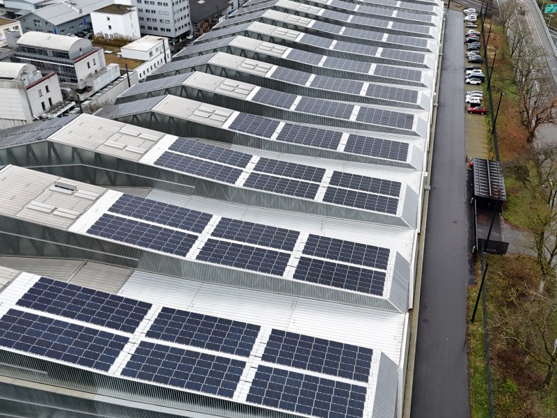 Aerial view of rows of solar panels installed on metal-roofed factory buildings.