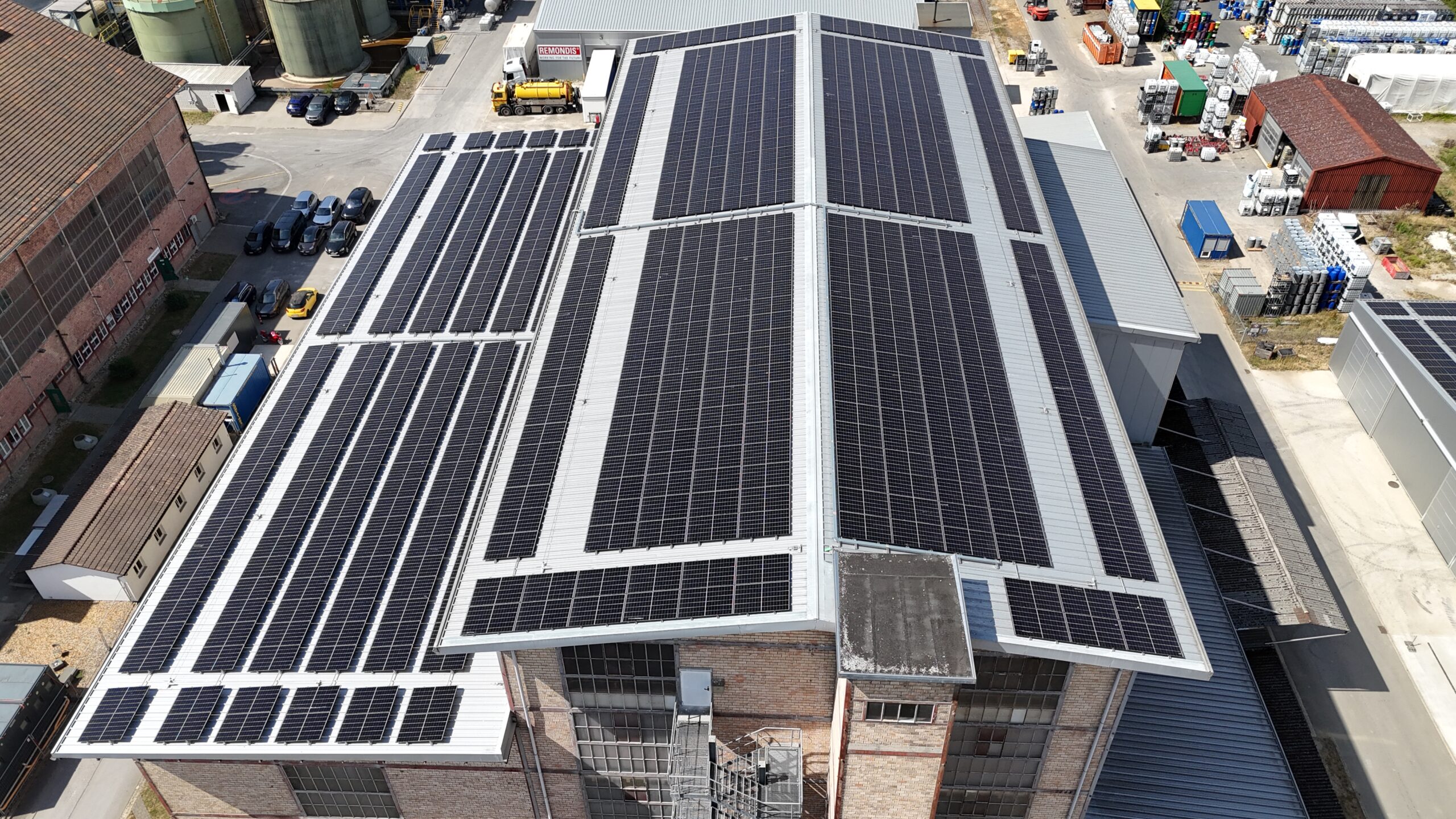 Aerial view of an industrial complex with extensive solar panels covering multiple roof surfaces for solar energy generation.