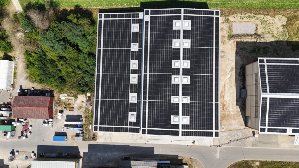Aerial view of large buildings with expansive solar panels on their rooftops, surrounded by trees and a road nearby.
