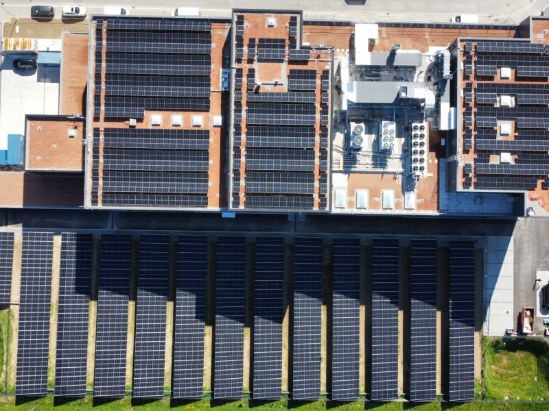 Aerial view of urban rooftops covered with solar panels arranged in long rows across several buildings.
