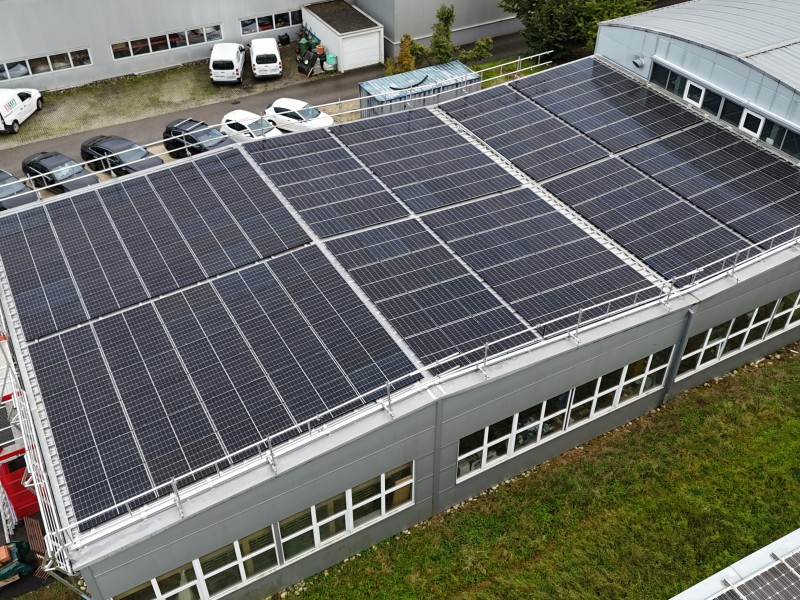 Aerial view of a flat-roof building covered with rows of dark solar panels on the roof area nearby a parking lot