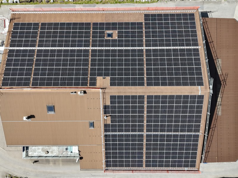 Aerial view of a brown roof covered with multiple rows of dark solar panels on a large building.