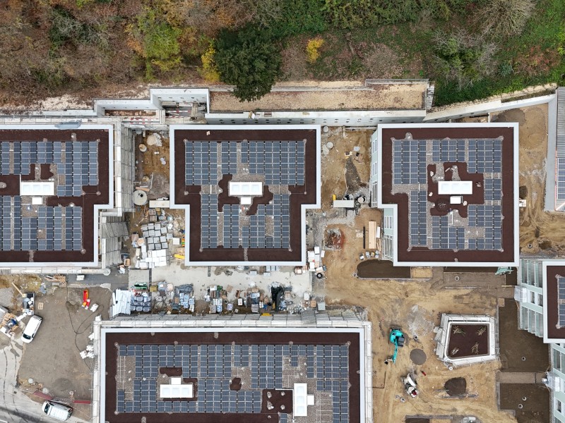 Aerial view of several flat-roof buildings covered with solar panels under construction or installation.