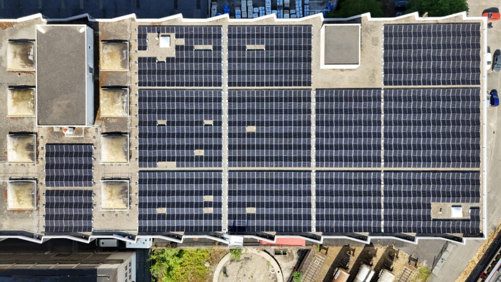 Aerial view of a roof covered with numerous dark solar panels arranged in neat rows and rectangular blocks.