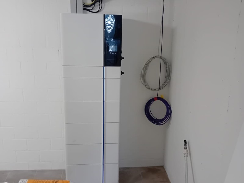 Tall white equipment cabinet with a blue vertical stripe in a utility room, with gray and purple cables coiled on the wall nearby.