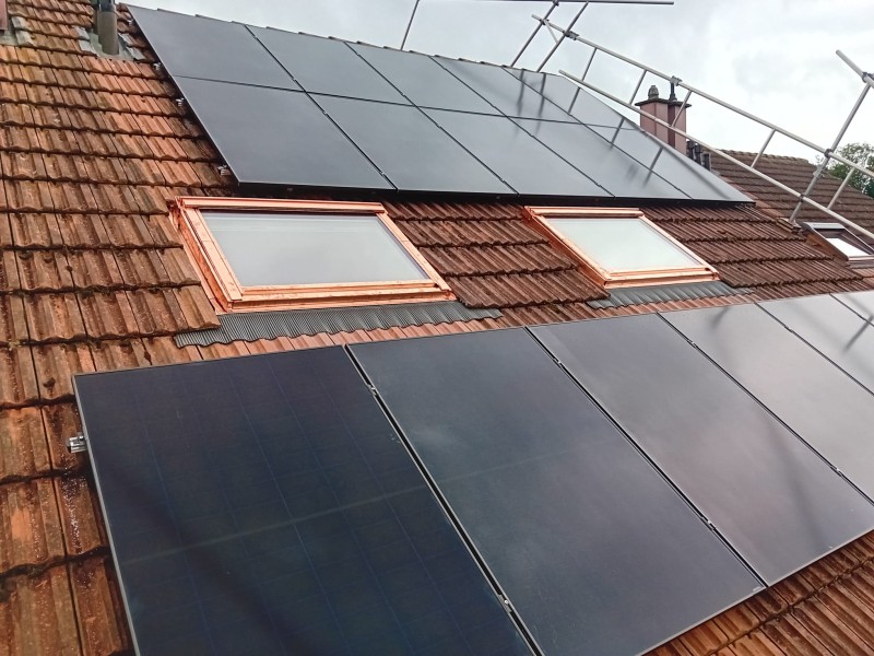 Solar panels on a red-tiled roof with two skylights, mounted to generate electricity from sunlight.