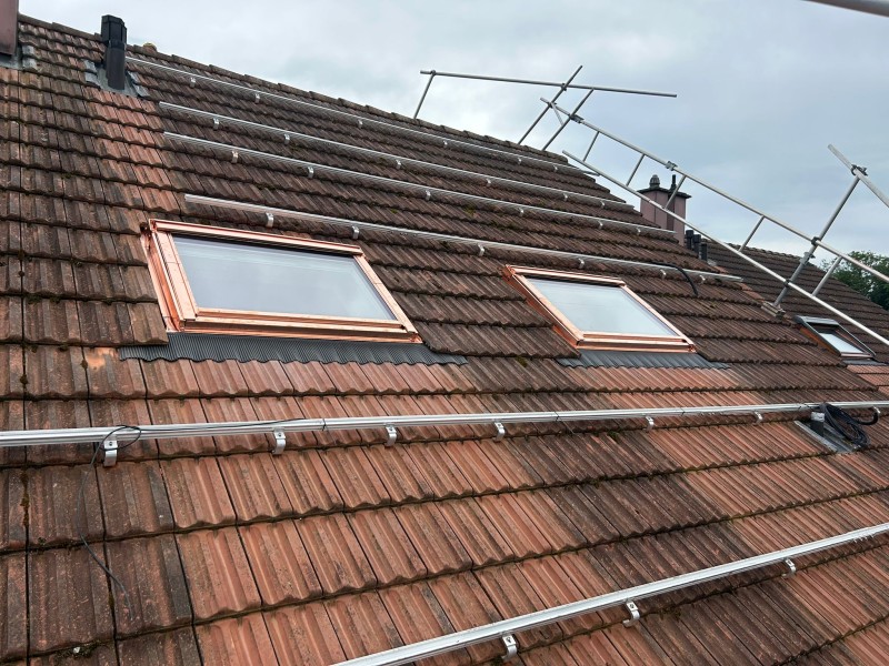 Roof with two skylight windows and metal antenna masts on a cloudy day.