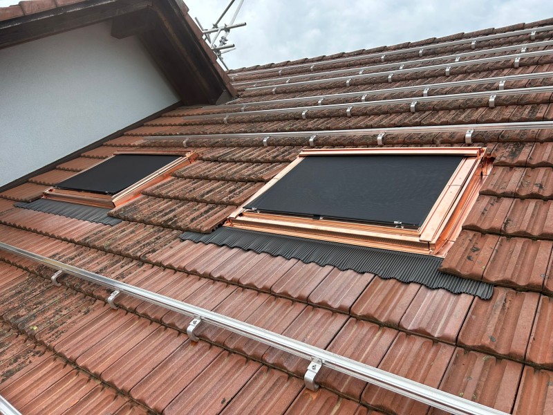 Red clay tile roof with two copper-framed skylights installed.