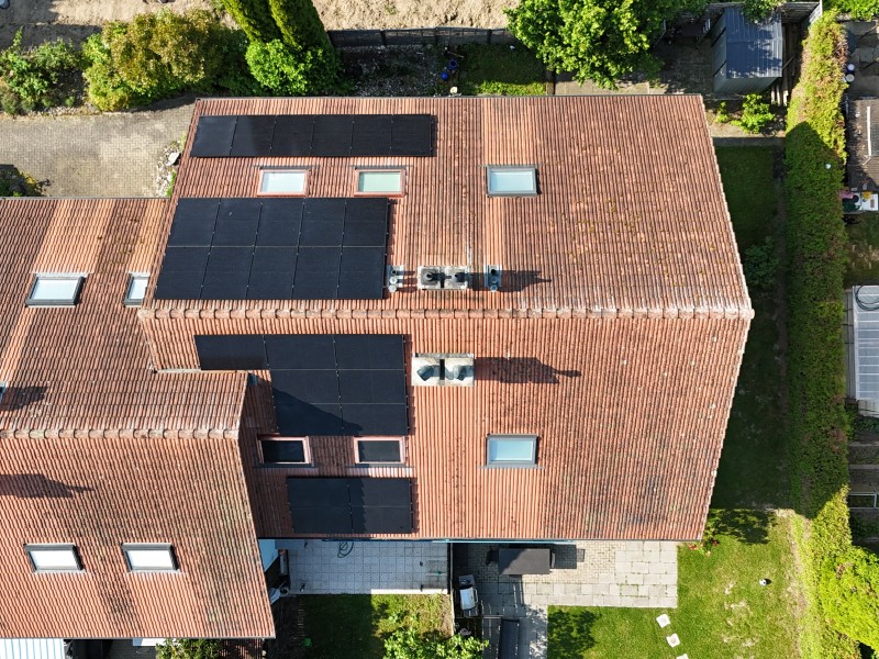 Aerial view of a red-tiled roof house with several large black solar panels on the roofcape
