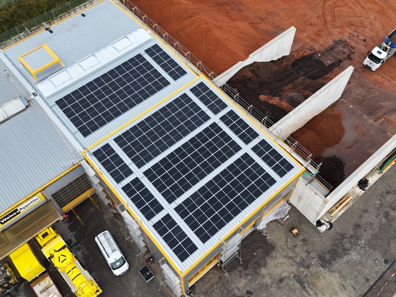 Aerial view of a building roof with large solar panels next to a construction site readied with dirt and equipment nearby, showing a truck in the yard.