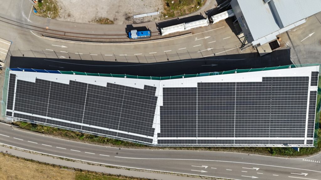 Aerial view of a large rooftop covered with solar panels beside a road and tram tracks at a loading=