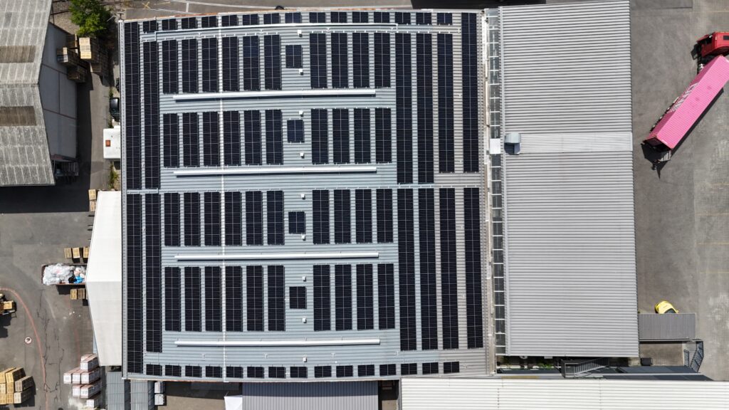 Aerial view of a large industrial roof densely covered with solar panels; loading=