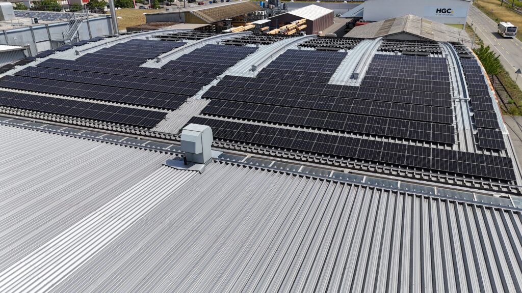 Solar panels covering a curved metal warehouse roof in neat rows, capturing a large rooftop PV array.