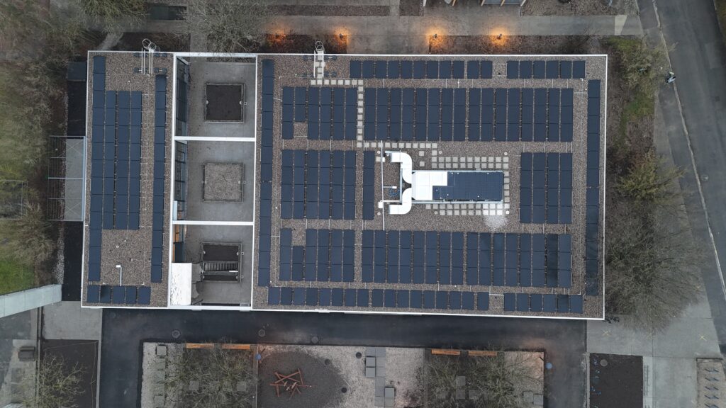 Aerial view of a flat-roofed building covered with rows of solar panels in a grid pattern.