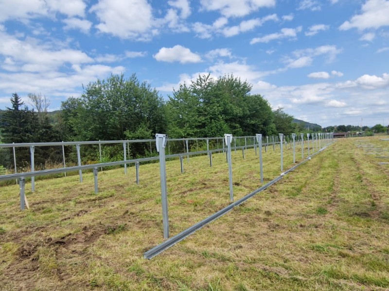 Metal solar panel mounting racks installed in a grassy field, extending into the distance under a blue sky with clouds.