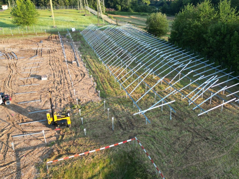 Aerial view of a solar farm under construction with long rows of steel mounting racks for solar panels and construction equipment on a cleared field.