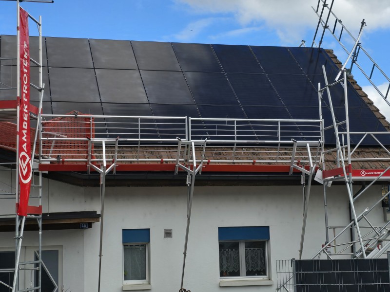 Scaffolding around a white house with a dark-tiled, solar-panel-covered roof.