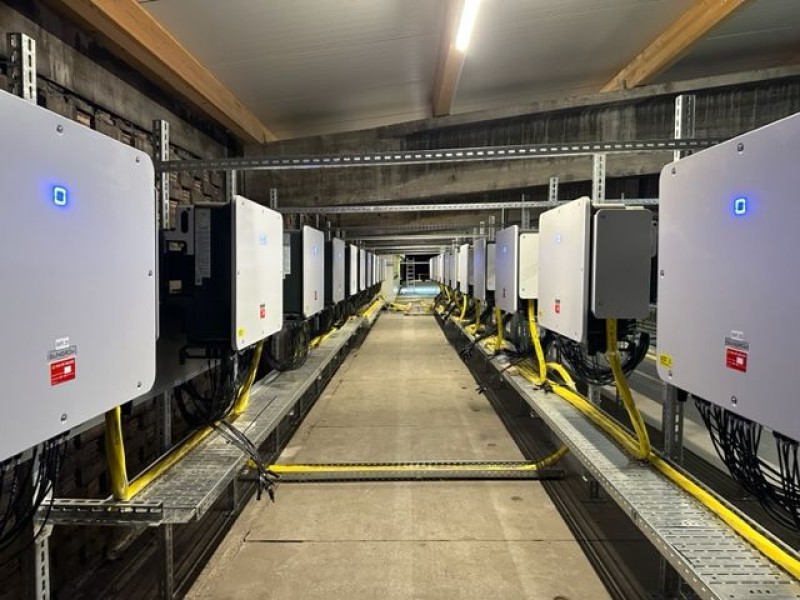 Row of white electrical cabinets with blue indicator lights in a data center aisle, yellow cables on raised racks.